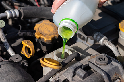 Hand with bottle pouring antifreeze coolant into the expansion tank. Ancillaries